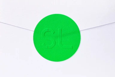 Vibrant green circular sticker with debossed letters SL on a white paper envelope flap