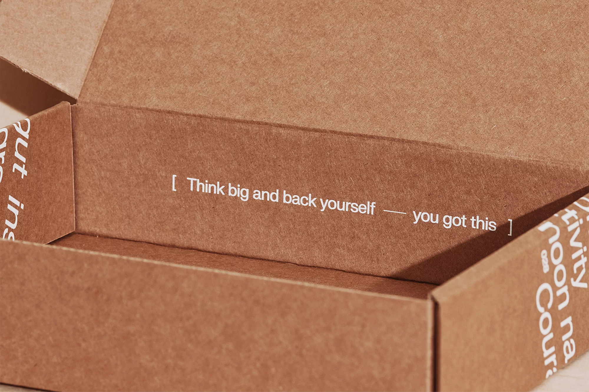 Open cardboard box interior featuring encouraging text: Think big and back yourself – you got this. Minimalist product shot.