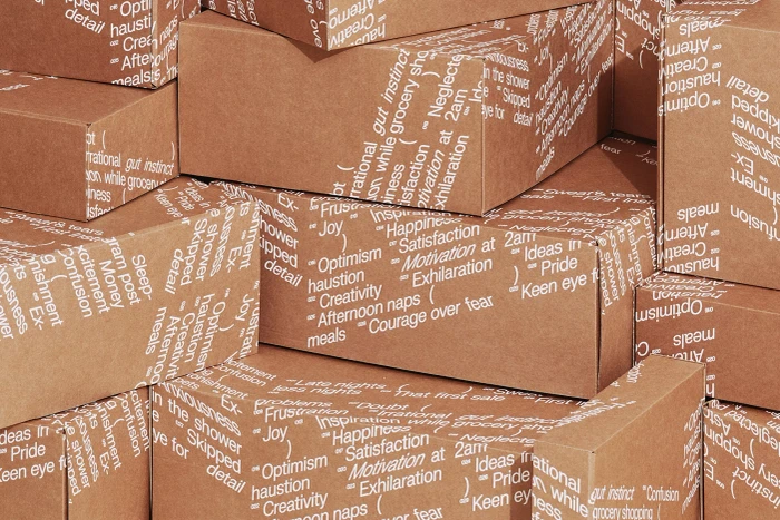 Stacked brown cardboard shipping boxes printed with white typographic patterns and words for Packhelp brand identity.