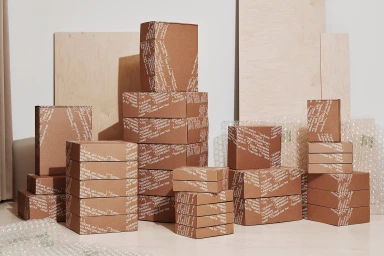 Stacks of branded brown cardboard boxes with typographic patterns displayed on a light surface.