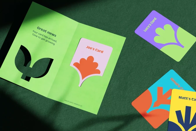 An opened, light-green greeting card with leaf cutouts, alongside colorful cards for Joe, Lucy, Simal, and Matt on a dark-green surface.