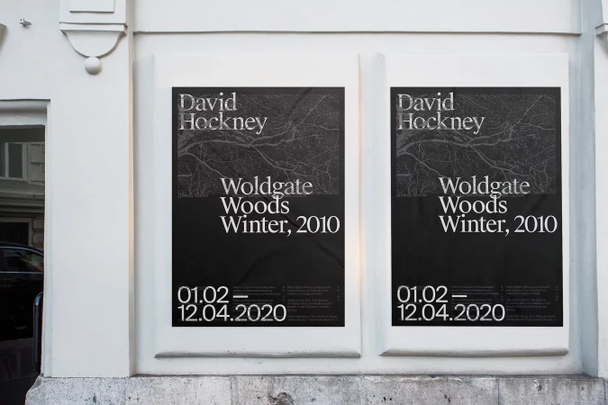 Two posters of David Hockney's Woldgate Woods Winter, 2010 exhibition are mounted on a white wall, capturing artistic expression and promotion.