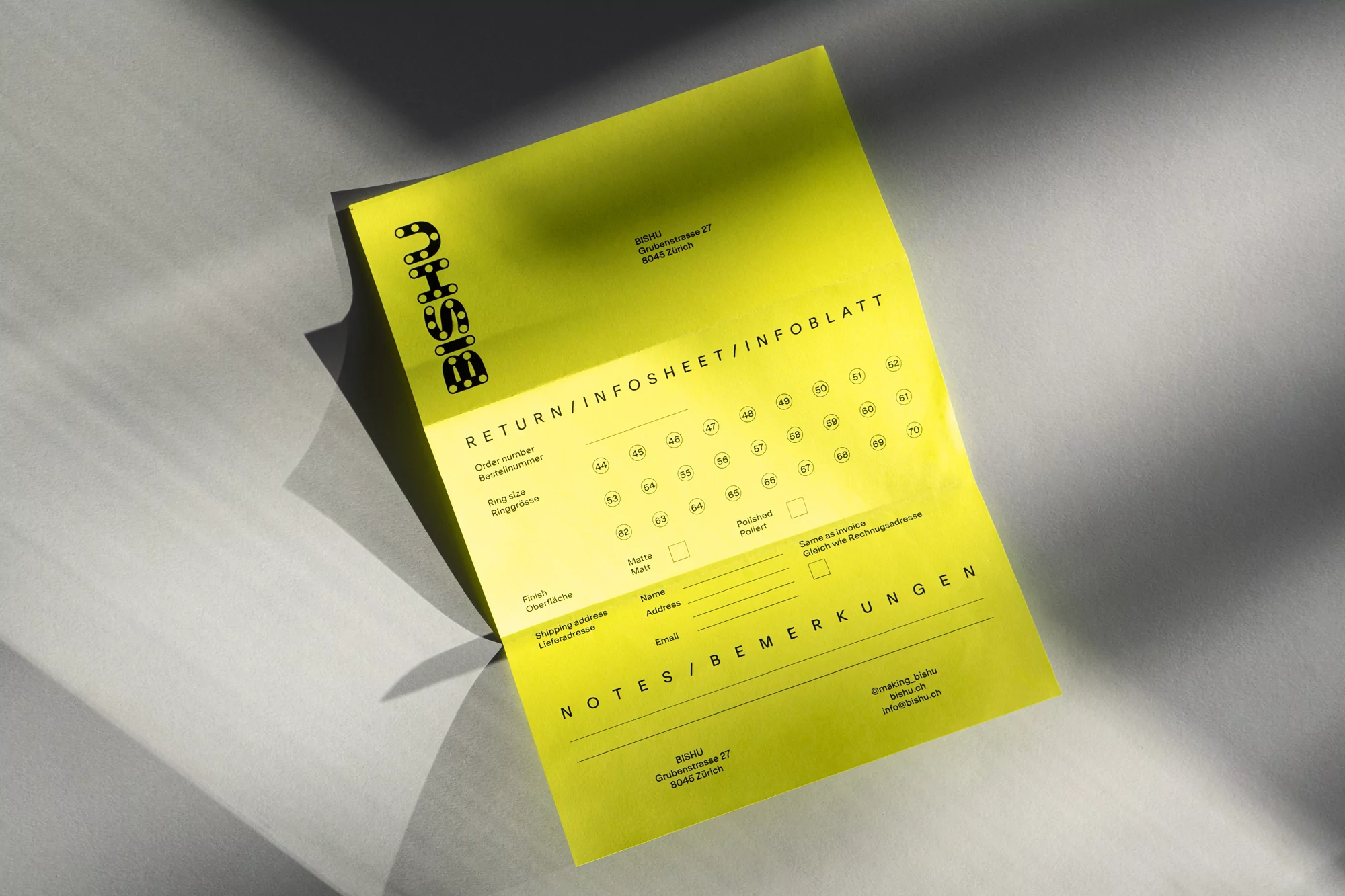 Graphic image featuring a bright yellow information sheet from the brand Bishu, laid on a textured gray surface in natural light.