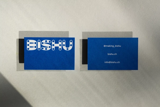 Two blue business cards with the name BISHU in white, featuring a modern, dotted design on a textured, neutral background.