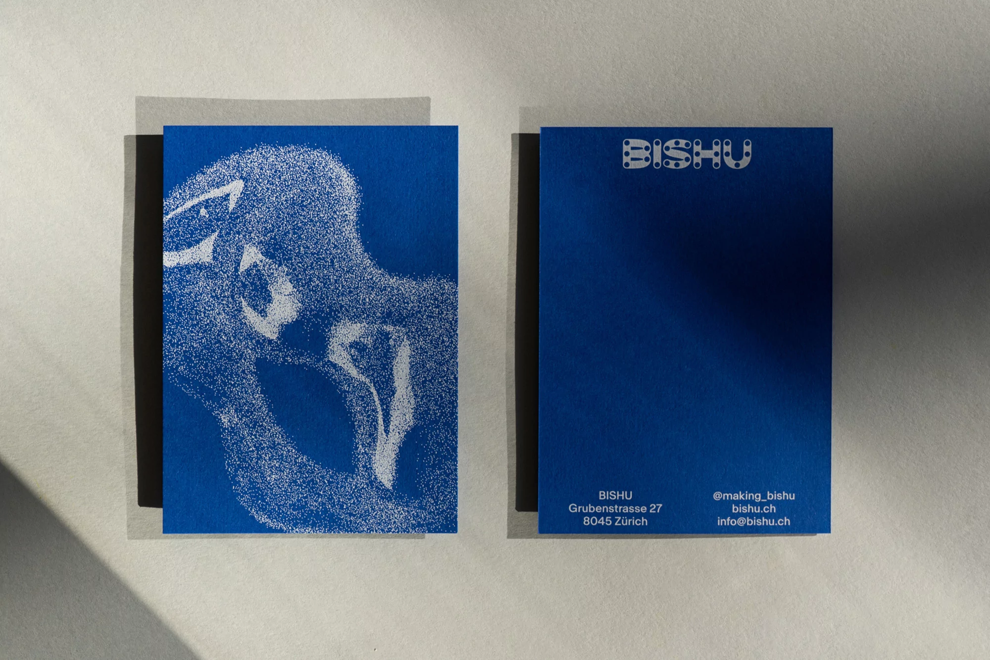 Two bright blue cards, one with a white speckled human figure illustration, the other with silver text and logo on a neutral background.