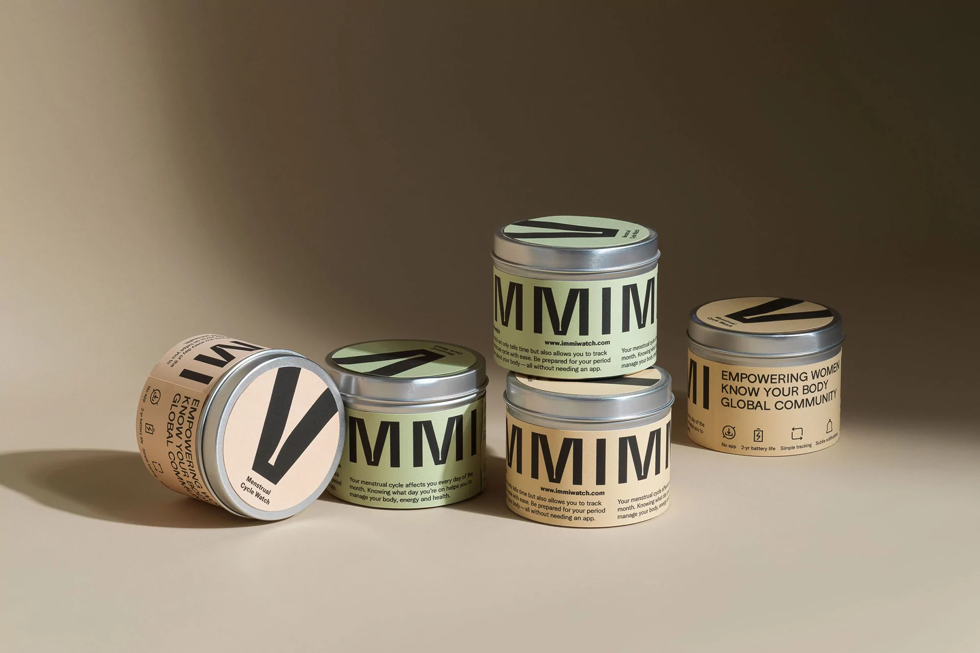 Product shot of MMIM menstrual cycle watch tins in tan and green colors, arranged on a neutral background. Wellness and femtech.