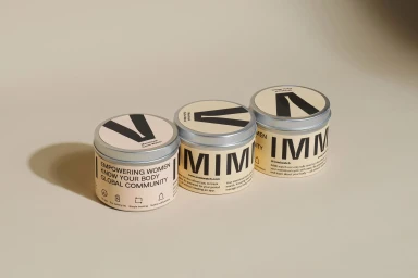 Three round branded product tins arranged diagonally on a neutral beige background with soft directional lighting