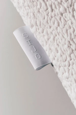 Close-up of a white textured fabric label featuring the embroidered brand name SIJO attached to a quilted textile.