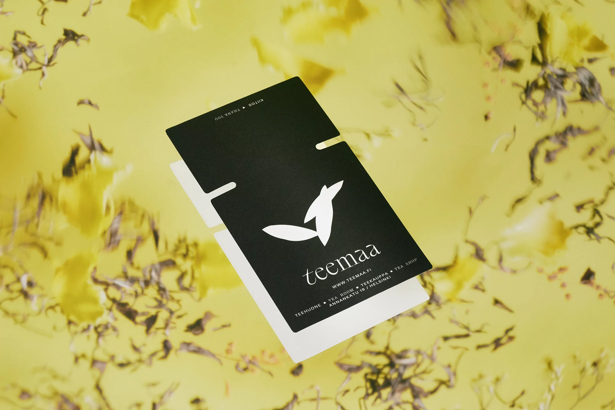 Elevated shot of a black and white Teemaa business card on a yellow background with a floral pattern.