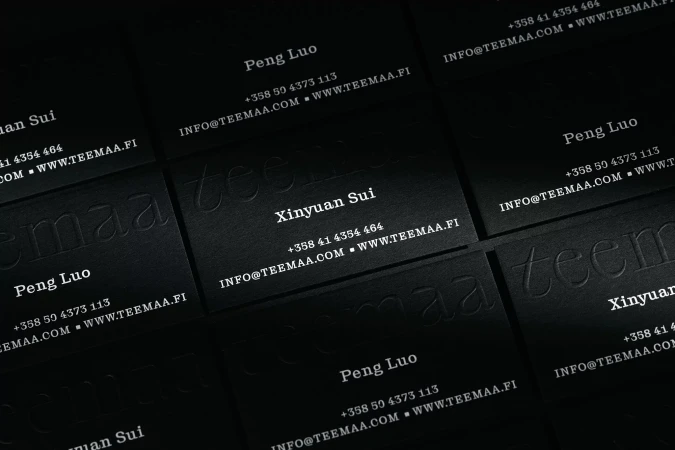 Several black business cards with white text, displaying contact information and names, arranged at a slight angle.
