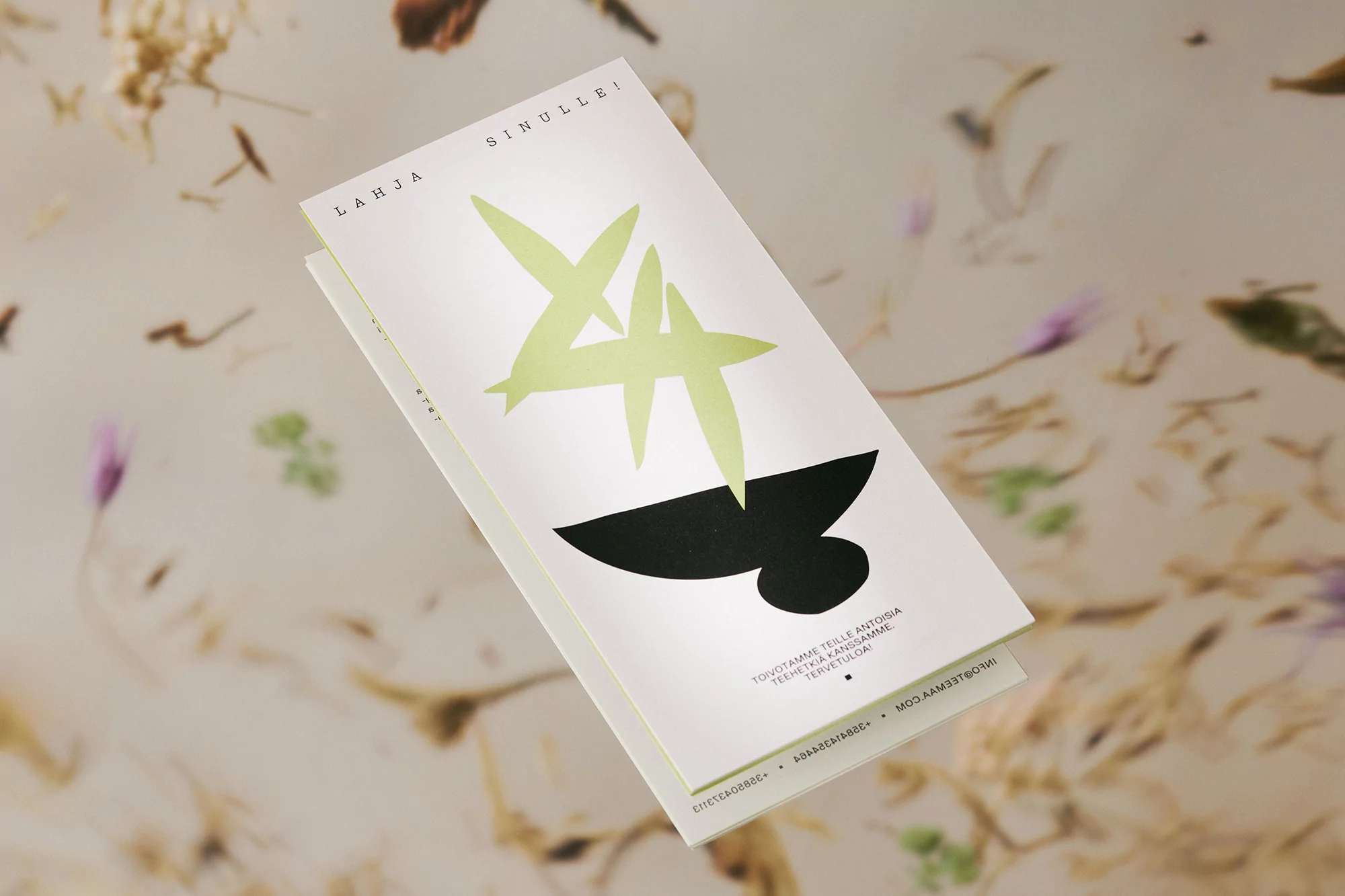 Minimalist graphic design on an invitation card featuring abstract shapes and botanical elements in a soft-focus background.