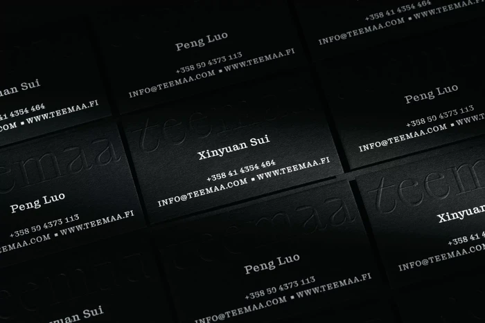 An arrangement of black business cards featuring embossed typography and white contact information details for TeaMaa.