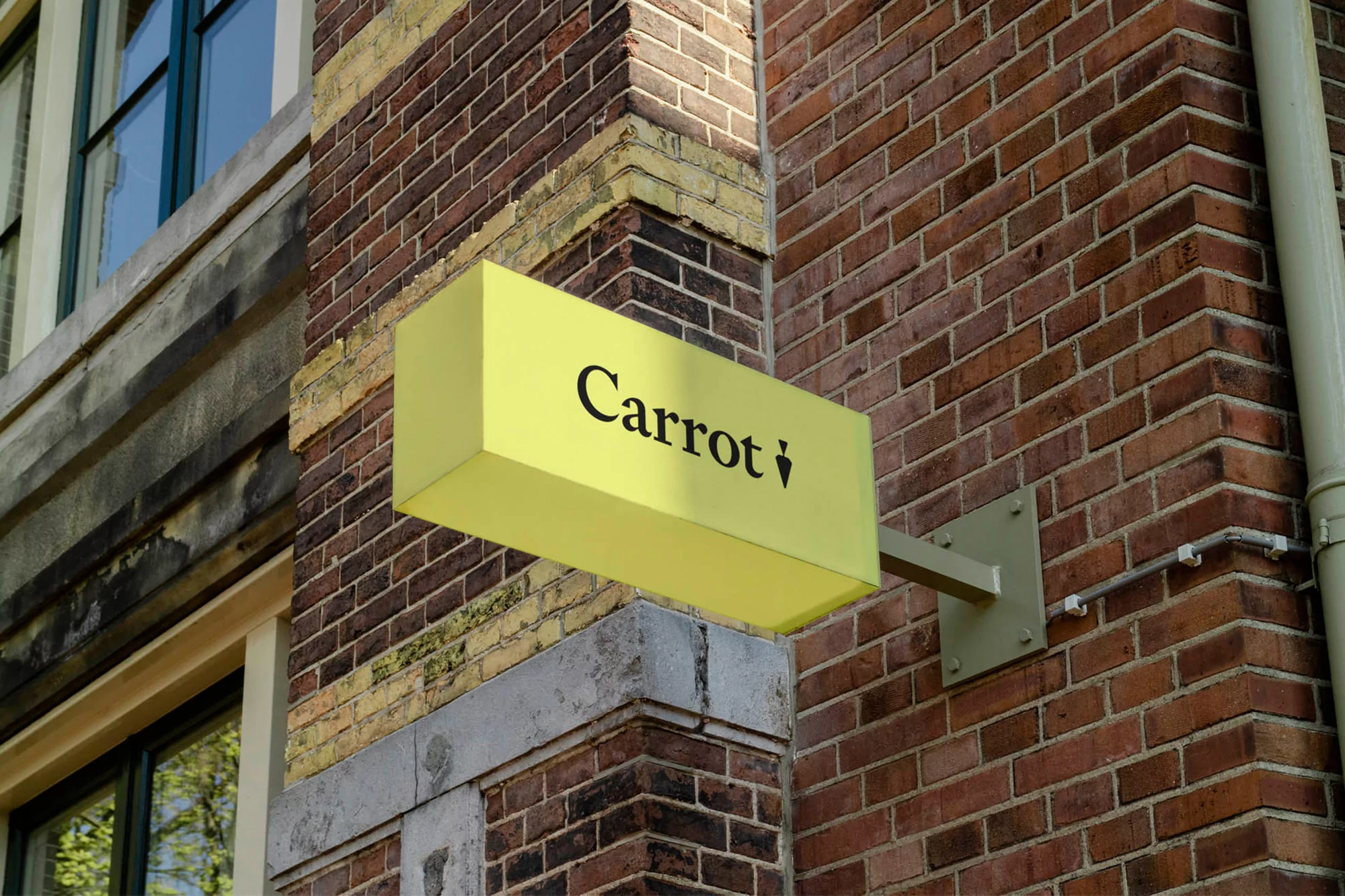 A yellow business sign with the word 'Carrot' in black letters is mounted on a brick building, capturing an urban setting and branding.