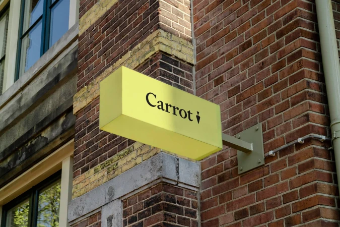 A yellow business sign with the word 'Carrot' in black letters is mounted on a brick building, capturing an urban setting and branding.