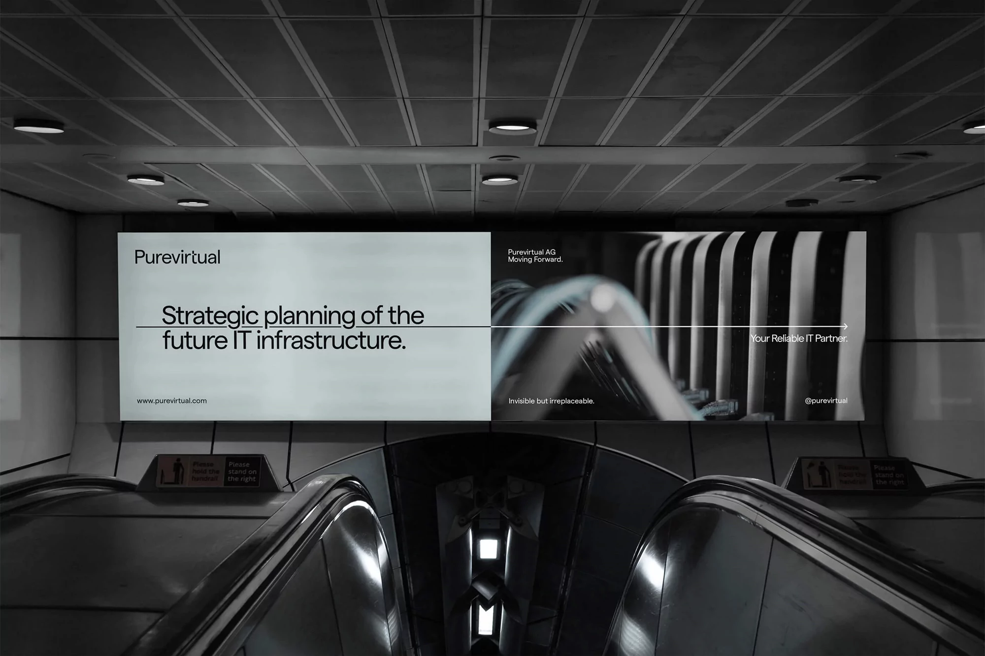 Illuminated advertising billboard for Purevirtual IT services above escalators in a modern subway or airport terminal setting.