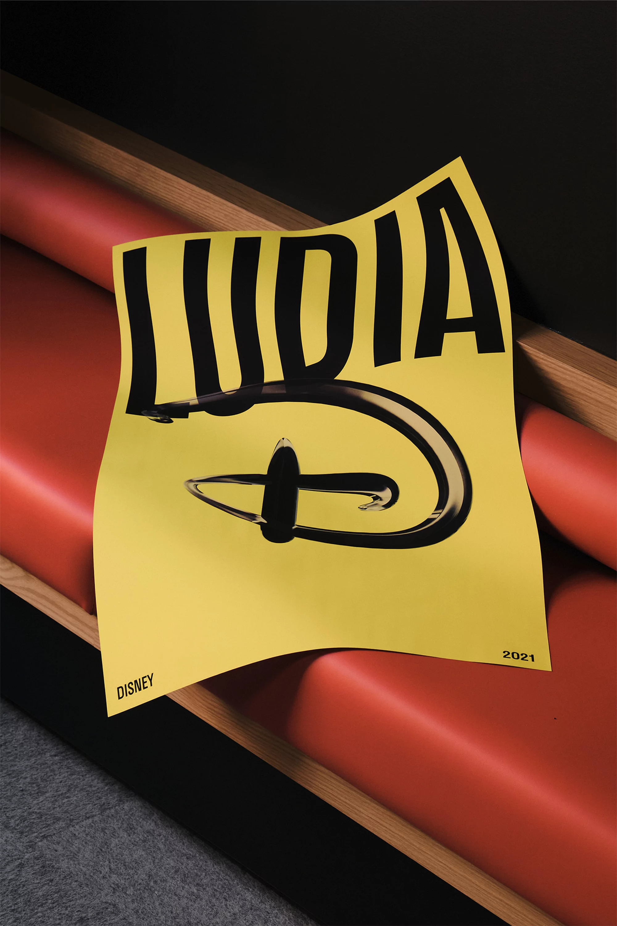 Promotional material featuring Disney logo on yellow paper, partially folded and leaning against a red and wooden bench indoors.
