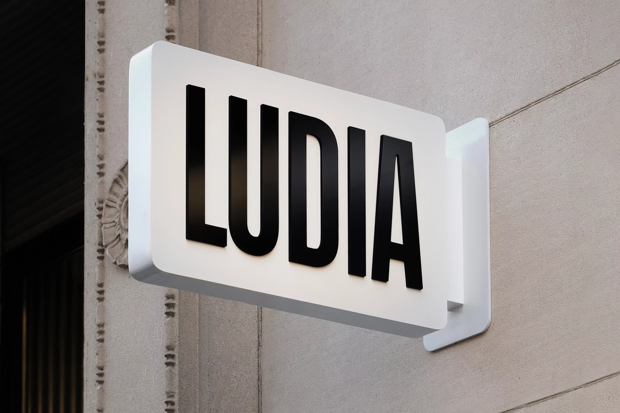 Exterior shot of the LUDIA brand sign mounted to the side of a building, featuring a white background and bold black lettering.