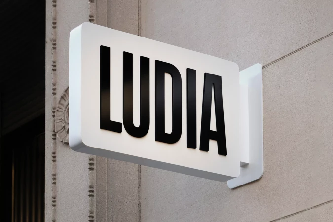 Exterior shot of the LUDIA brand sign mounted to the side of a building, featuring a white background and bold black lettering.