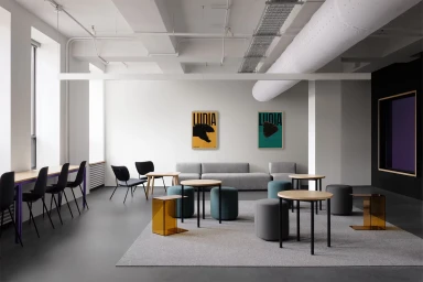 Modern minimalist office interior with grey concrete floors, round tables, grey modular seating, and framed brand posters on the wall.
