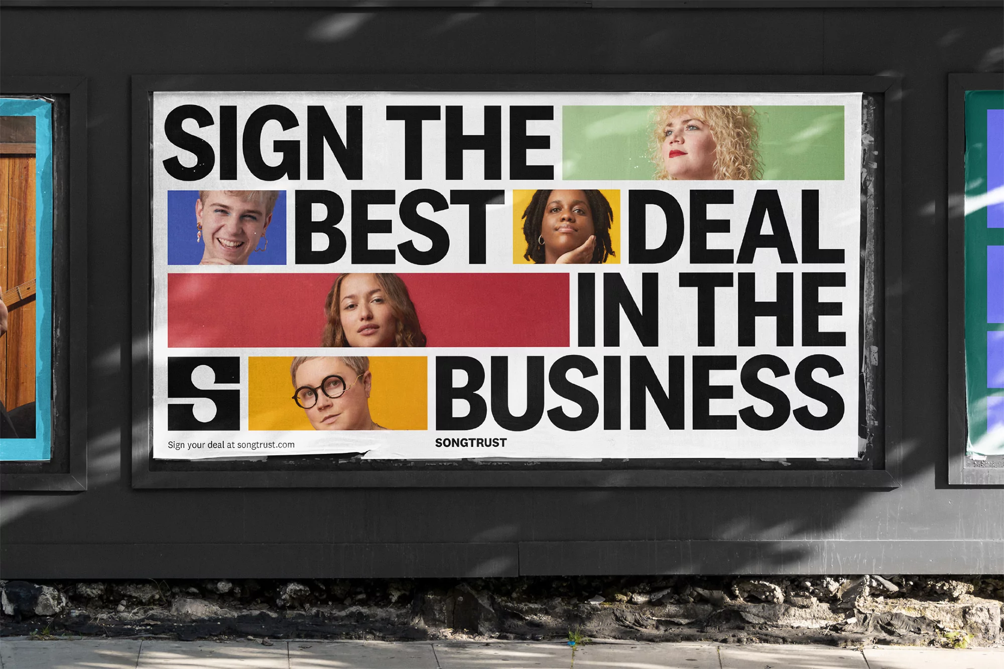 Outdoor billboard featuring diverse faces, bold text, and the SONGTRUST logo, set against a grey wall with stone accents below.