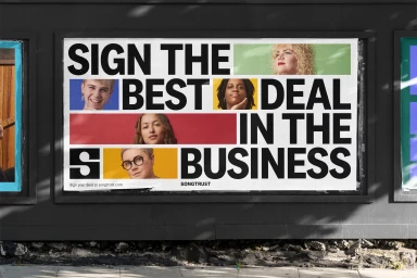 Songtrust billboard featuring bold black typography and photographic portraits on a dark street wall