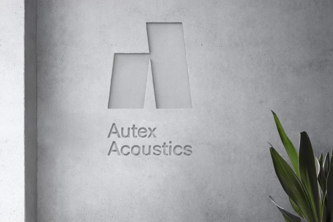 Concrete wall with the carved Autex Acoustics logo and live green plant adding a natural element to the minimalist interior design.