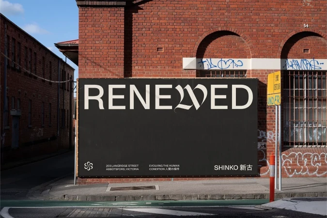 Urban black billboard featuring the word 'Renewed' in stylized white font, along with brand information and address details on brick building backdrop.