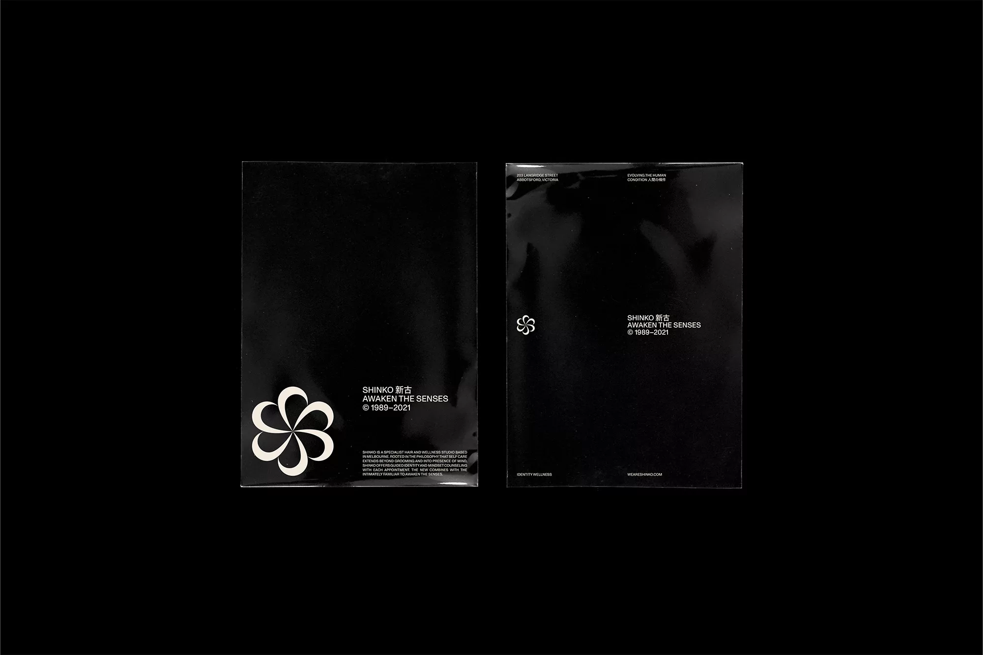 Two black booklets featuring minimalistic white typography and floral graphic elements, photographed against a solid black backdrop.