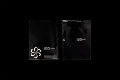 Two black glossy packaging bags featuring white typography and floral logo for brand Shinko against a black background