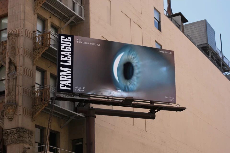 Outdoor billboard advertising Farm League and UCSF featuring a macro image of a human eye in San Francisco. Architectural background.