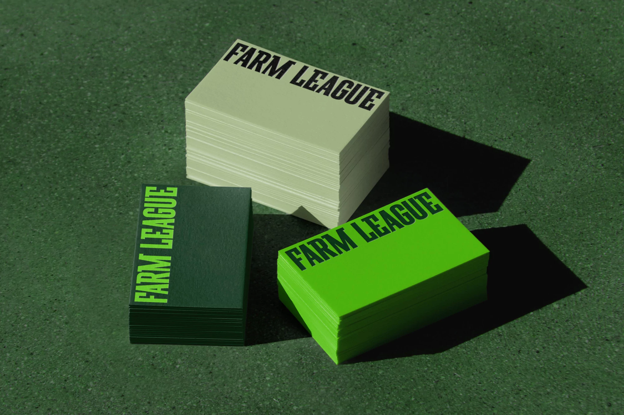 Three stacks of business cards with 'Farm League' printed on them in different shades of green, resting on a matching green surface.