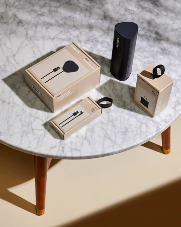 Still life product shot of Sonos charging station components, featuring packaging and a black triangular wireless charging stand on a marble table.