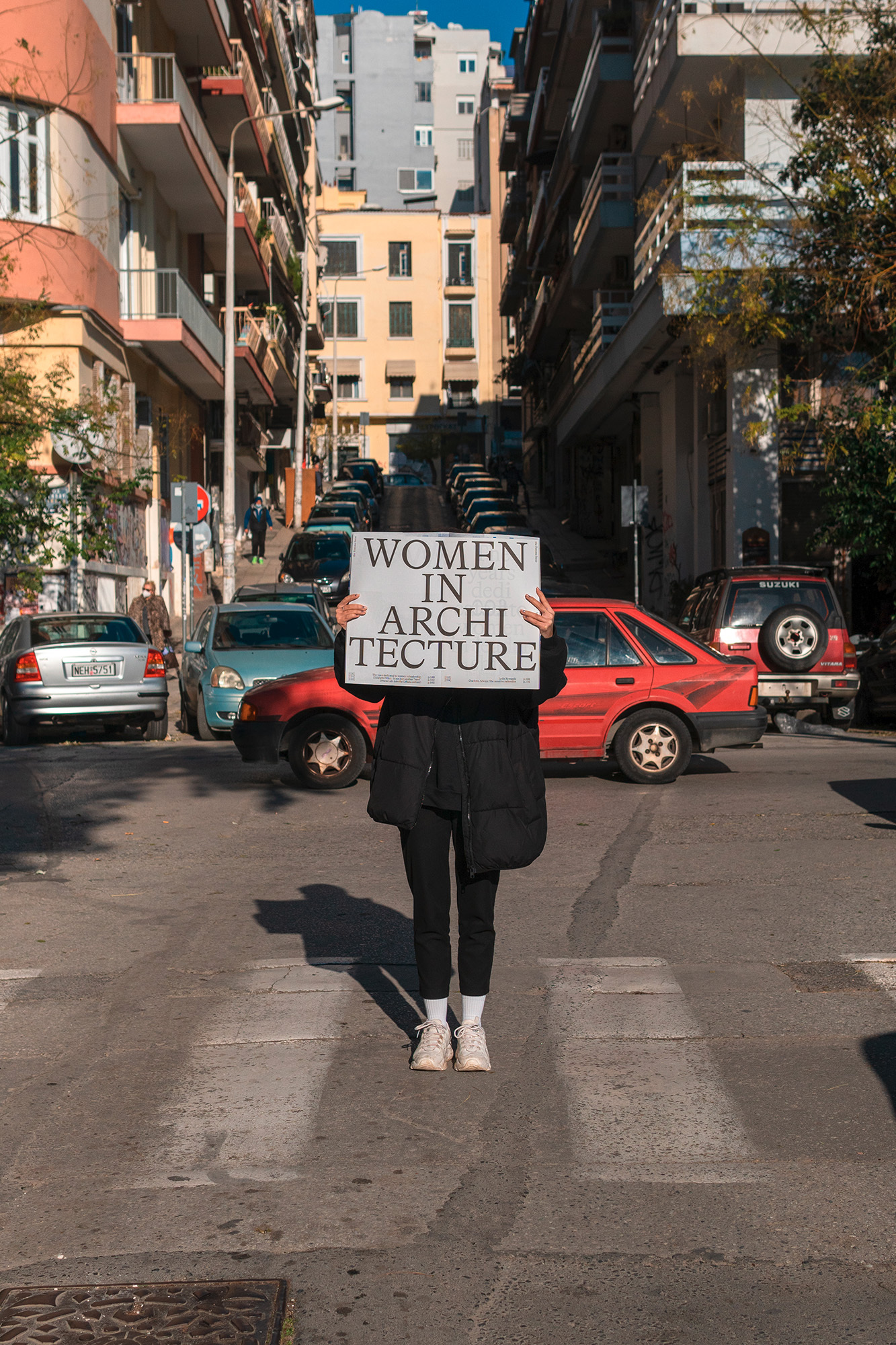 Person holding a sign reading Women in Architecture while standing on a crosswalk in a dense urban street.