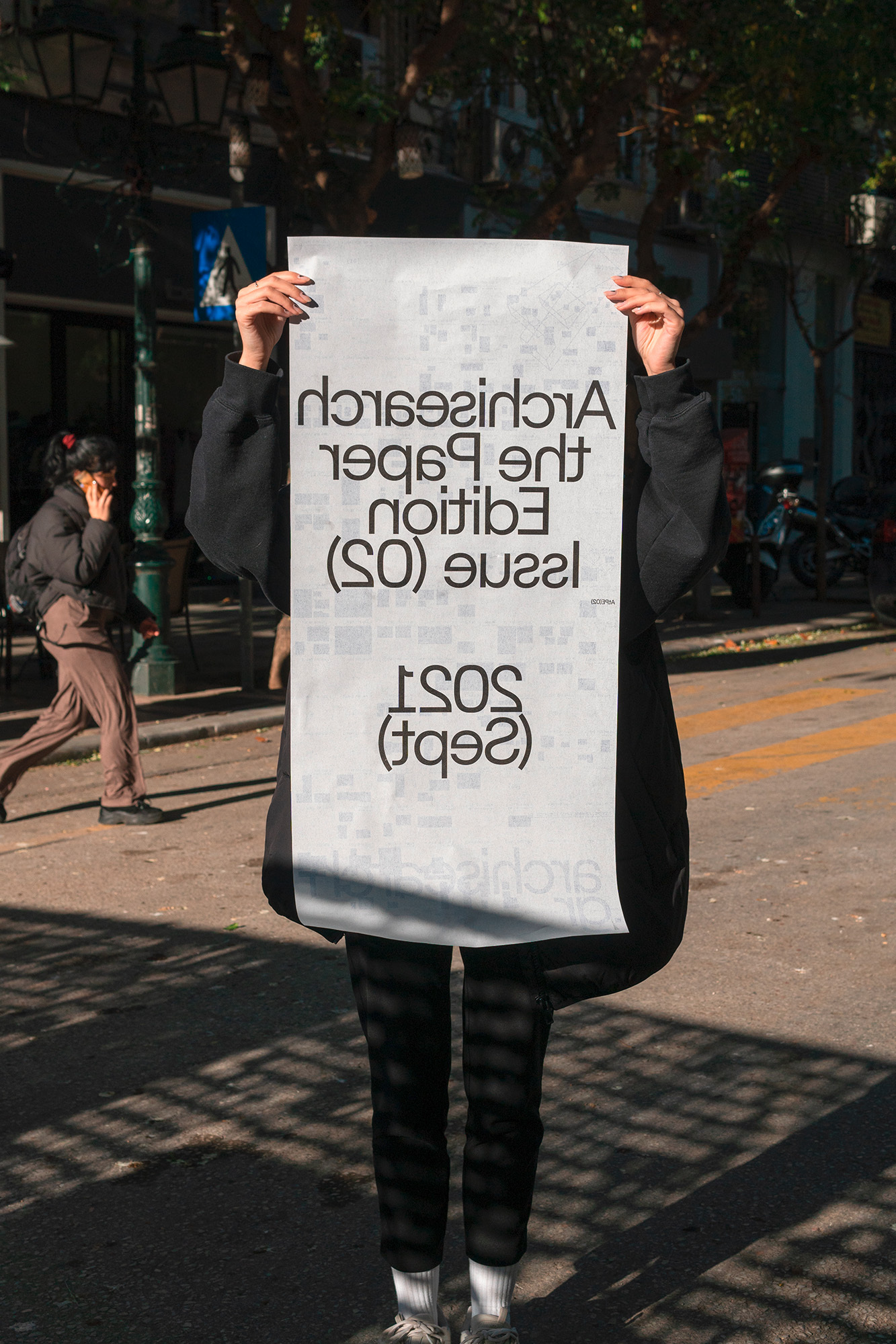 Person holding large printed paper poster with typography on a sunny city street