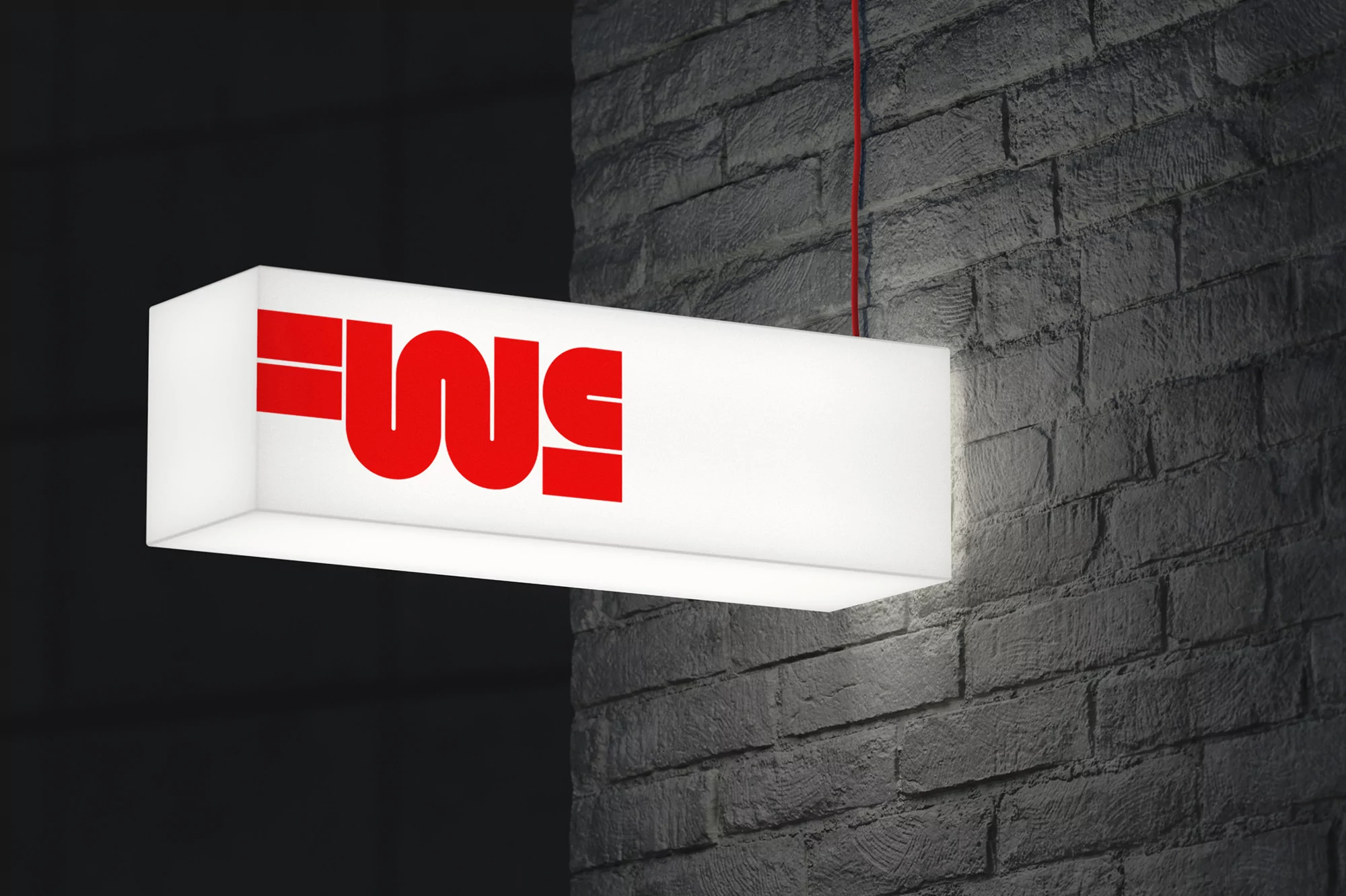 Illuminated rectangular sign mounted on a grey brick wall with red text, hanging by a red wire in an indoor setting.