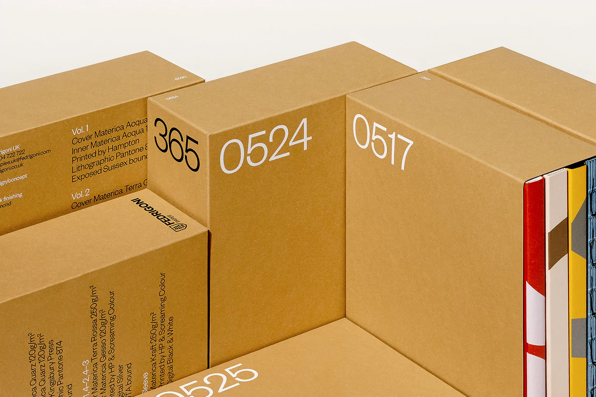 Stacks of Fedrigoni paper sample boxes in tan cardboard with printed brand and paper sample details, against a white background.