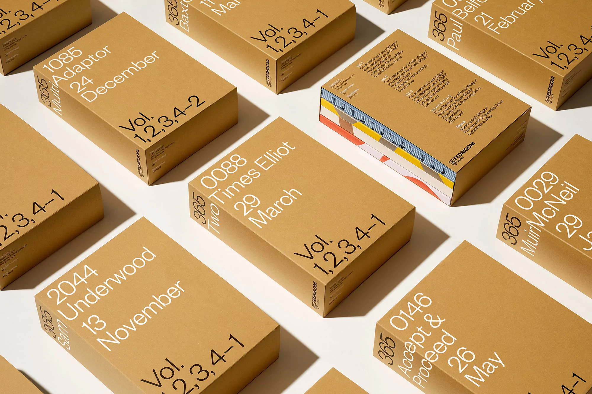 Stacks of Fedrigoni paper sample books with white text on brown paper, showcasing typography and design on a clean, white background.