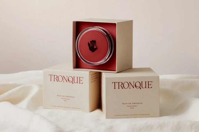 Cosmetics packaging featuring branded cream jars arranged symmetrically on a soft cream fabric background.