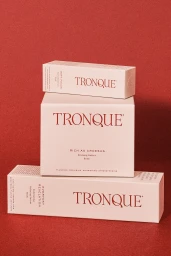 Stacked skincare boxes with Tronque branding resting against a deep red textured background surface.