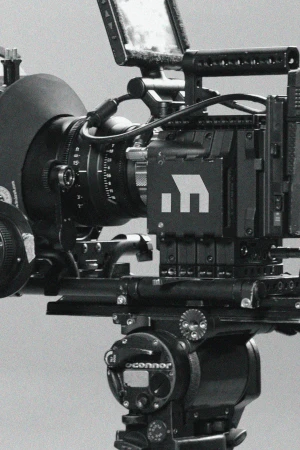 Professional black digital film camera on a tripod in a photography studio. The camera is large with an attached lens and monitor.