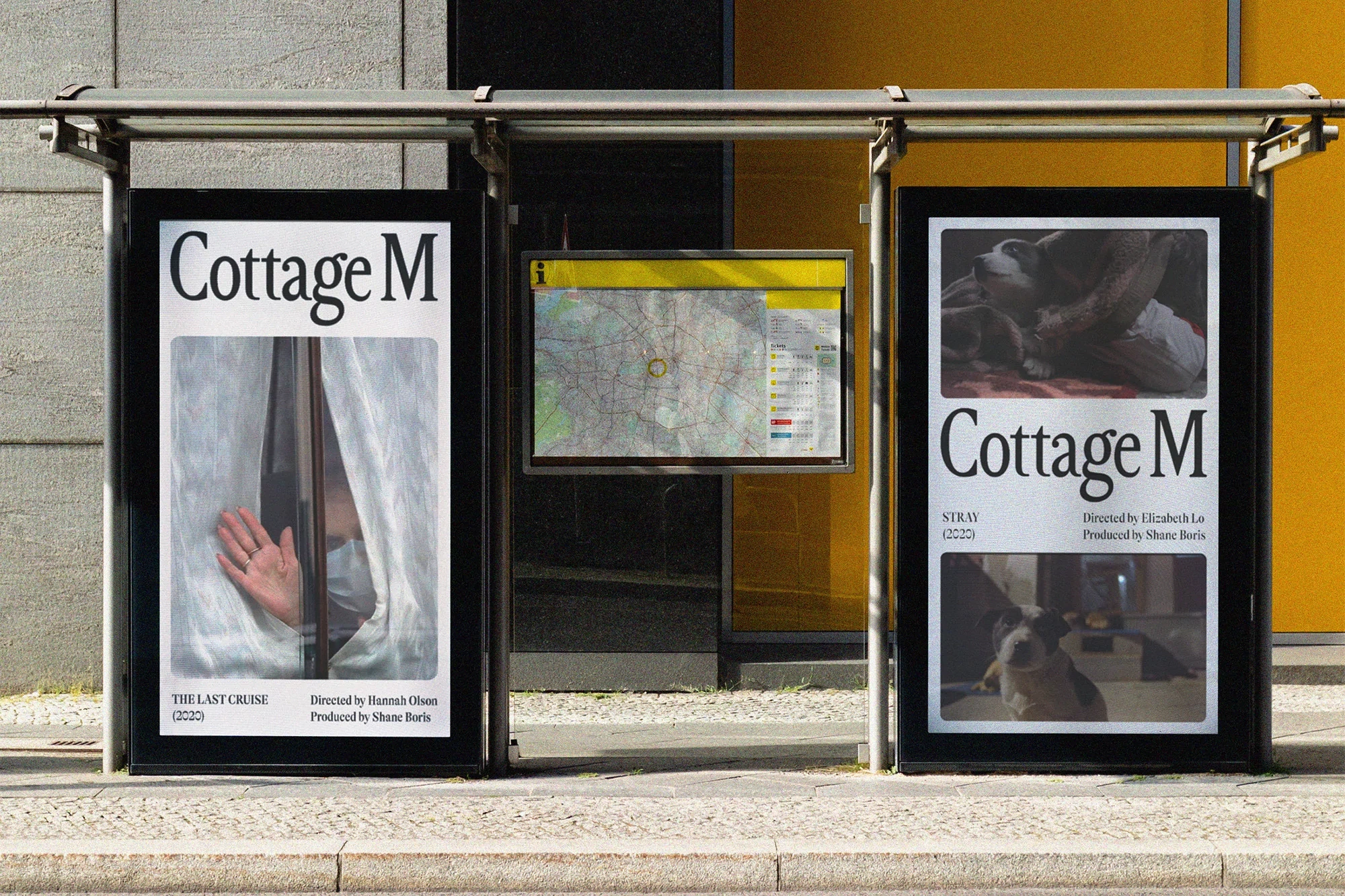 Two vertical advertising posters for Cottage M displayed in a glass shelter on a city sidewalk.