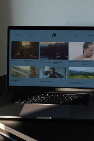 Laptop displaying a website interface with video thumbnails on a dark surface in dim room lighting