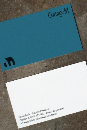 Business card for Cottage M featuring a slate blue front with a black logo and a white reverse side with contact details on stone.