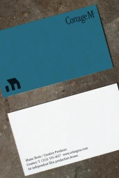 Business card for Cottage M featuring a slate blue front with a black logo and a white reverse side with contact details on stone.