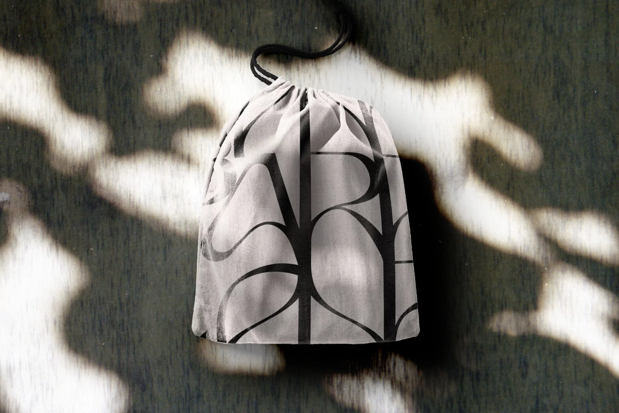 Drawstring bag with bold graphic print sitting on a mottled grey surface with dappled lighting and shadows, presented in portrait format.