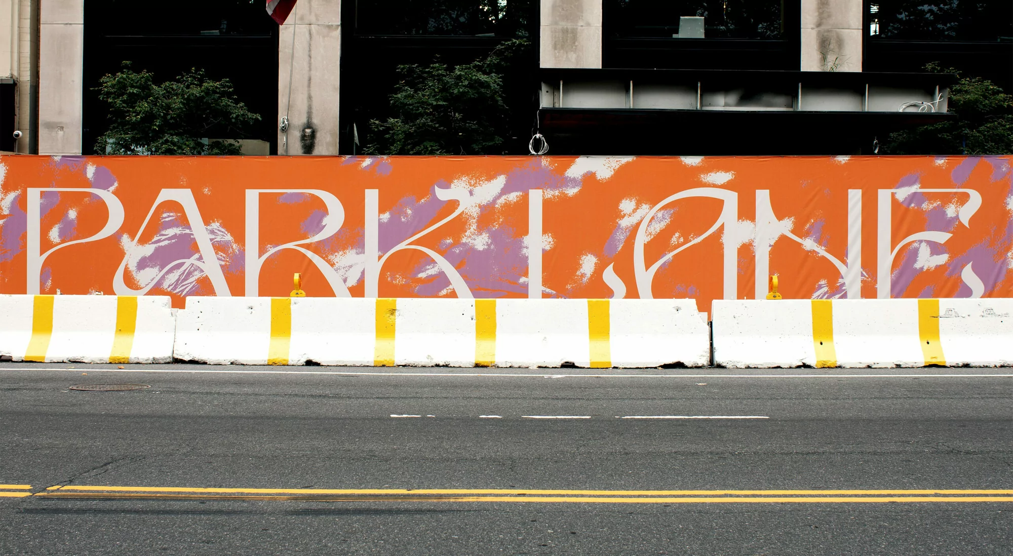 Urban scene featuring street-level view of asphalt road, concrete barriers with yellow stripes, and a large orange sign that reads PARKLANE.