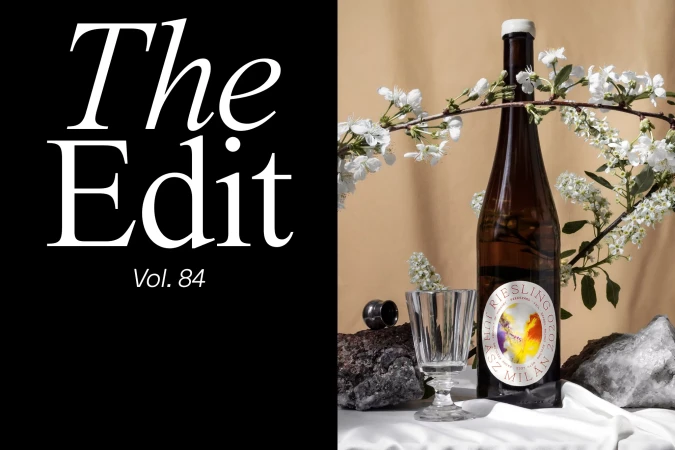 Still life photo of a wine bottle and glass on a white cloth with white flowers against a beige background next to black text.
