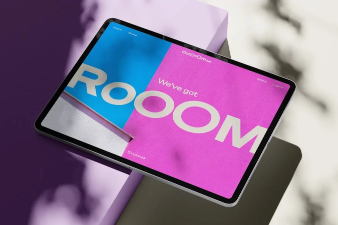 Tablet displays 'ROOM' graphic in pink and blue, sitting atop a purple geometric structure against a marble-patterned background.