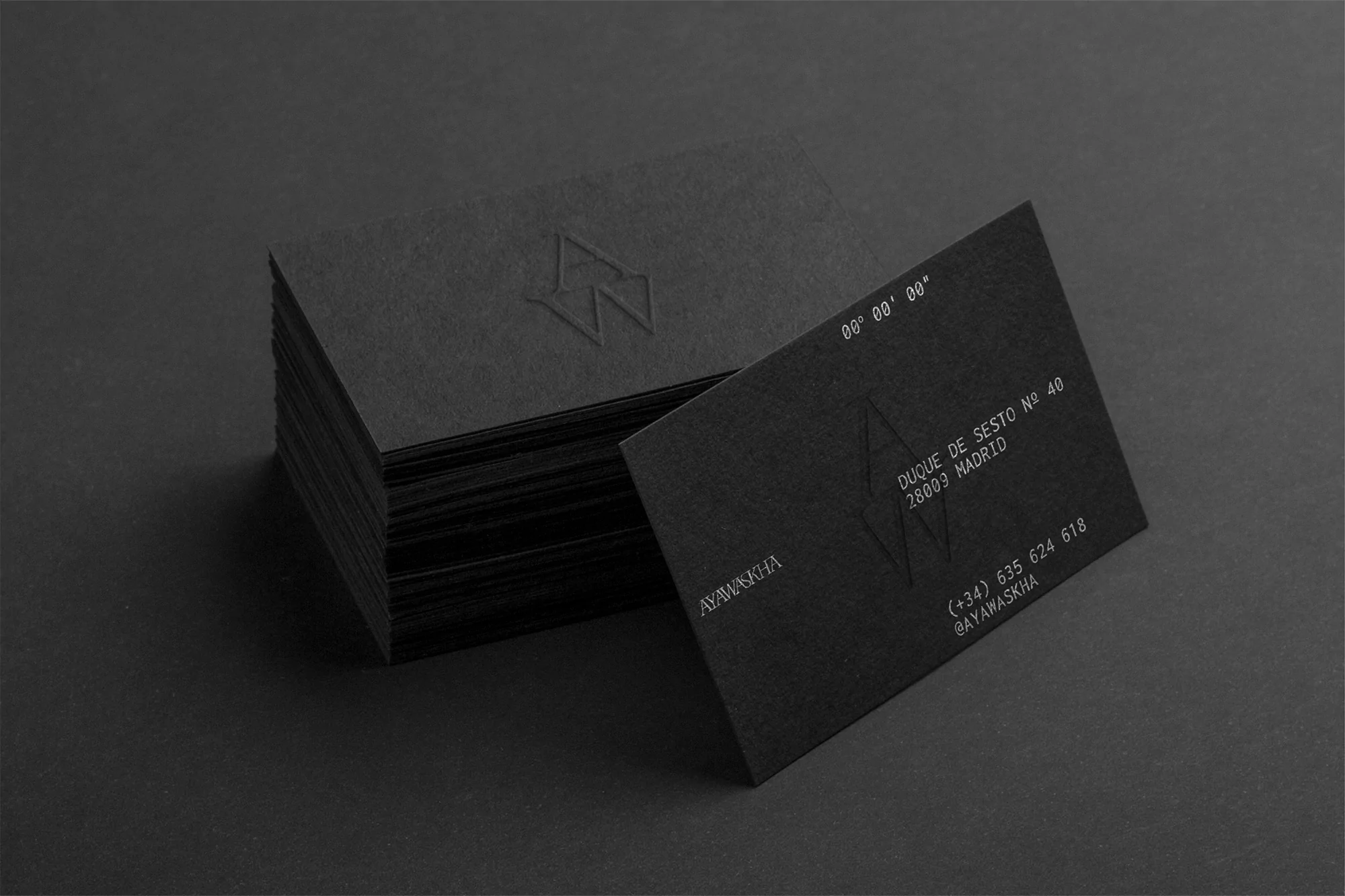 Stack of black business cards with minimalist design featuring embossed logo, company name, address, and contact information in grayscale.