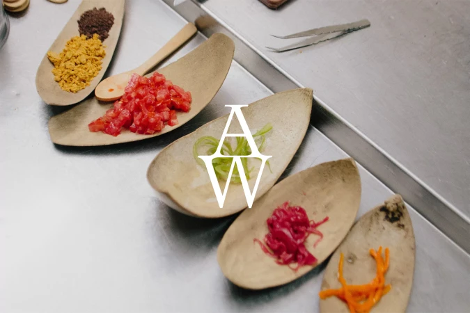 Overhead shot of wooden spoons filled with diced tomatoes, shredded vegetables, and spices on a stainless steel surface.